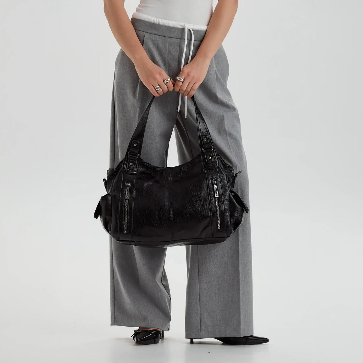Grand sac à main noir porté à la main avec un pantalon gris