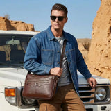 Homme portant un sac ordinateur Le Sac Bandoulière en cuir marron devant un 4x4 dans un paysage désertique