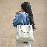 Sac cabas femme en cuir véritable blanc cassé porté à l’épaule sur fond beige